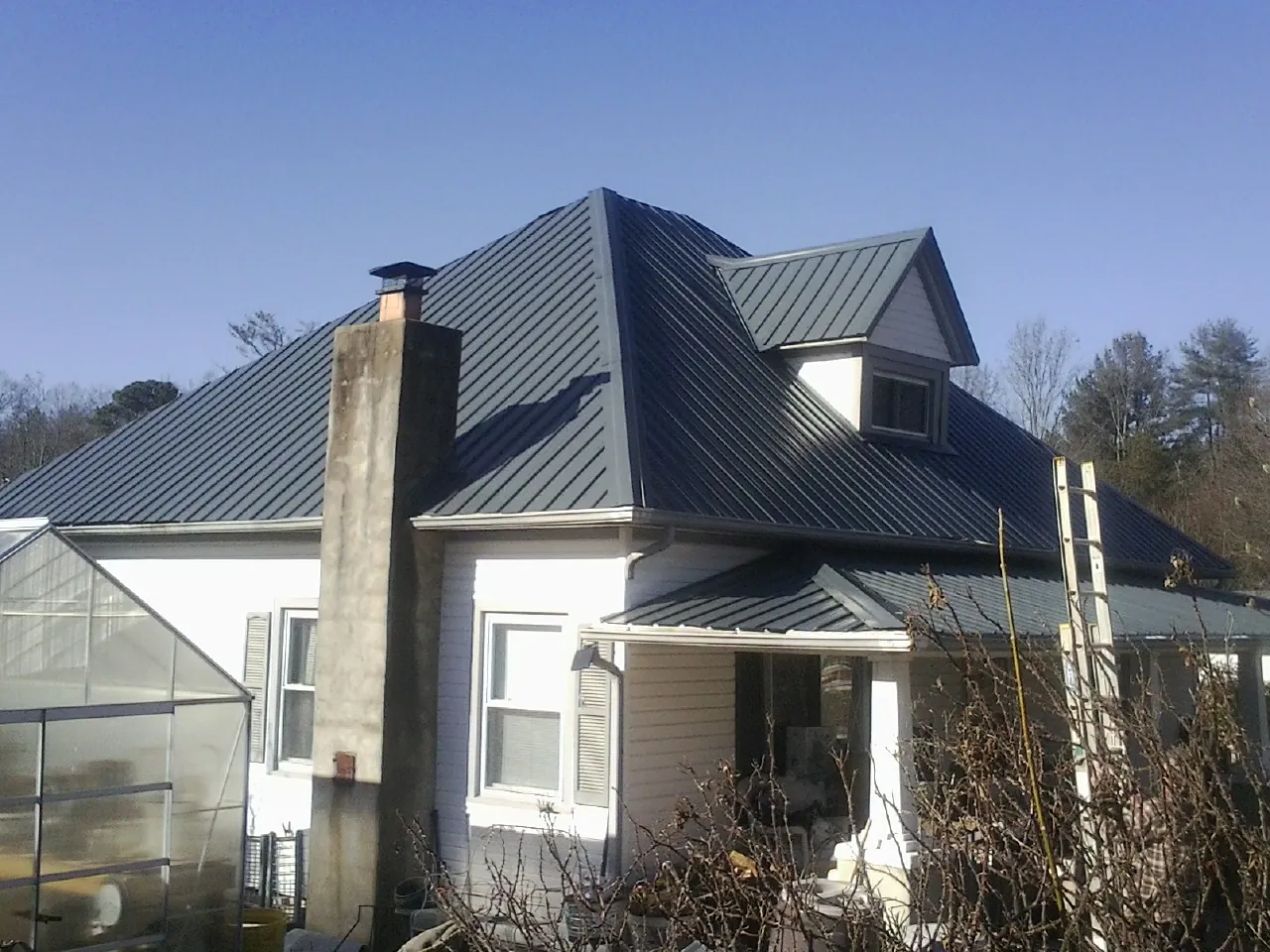 Dark blue standing seam metal roof on a white farmhouse with dormer — Slate & Tile Roof Repair by Roofing Brothers in Stafford
