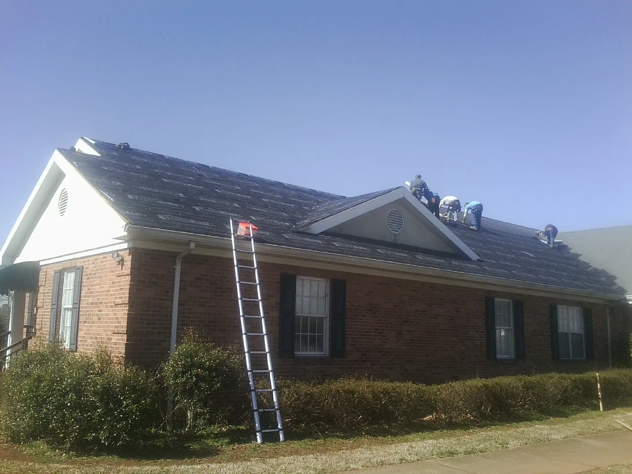 Crew tearing shingles off a brick ranch roof with a ladder set — Metal Roof Repair work by our crew in Stafford