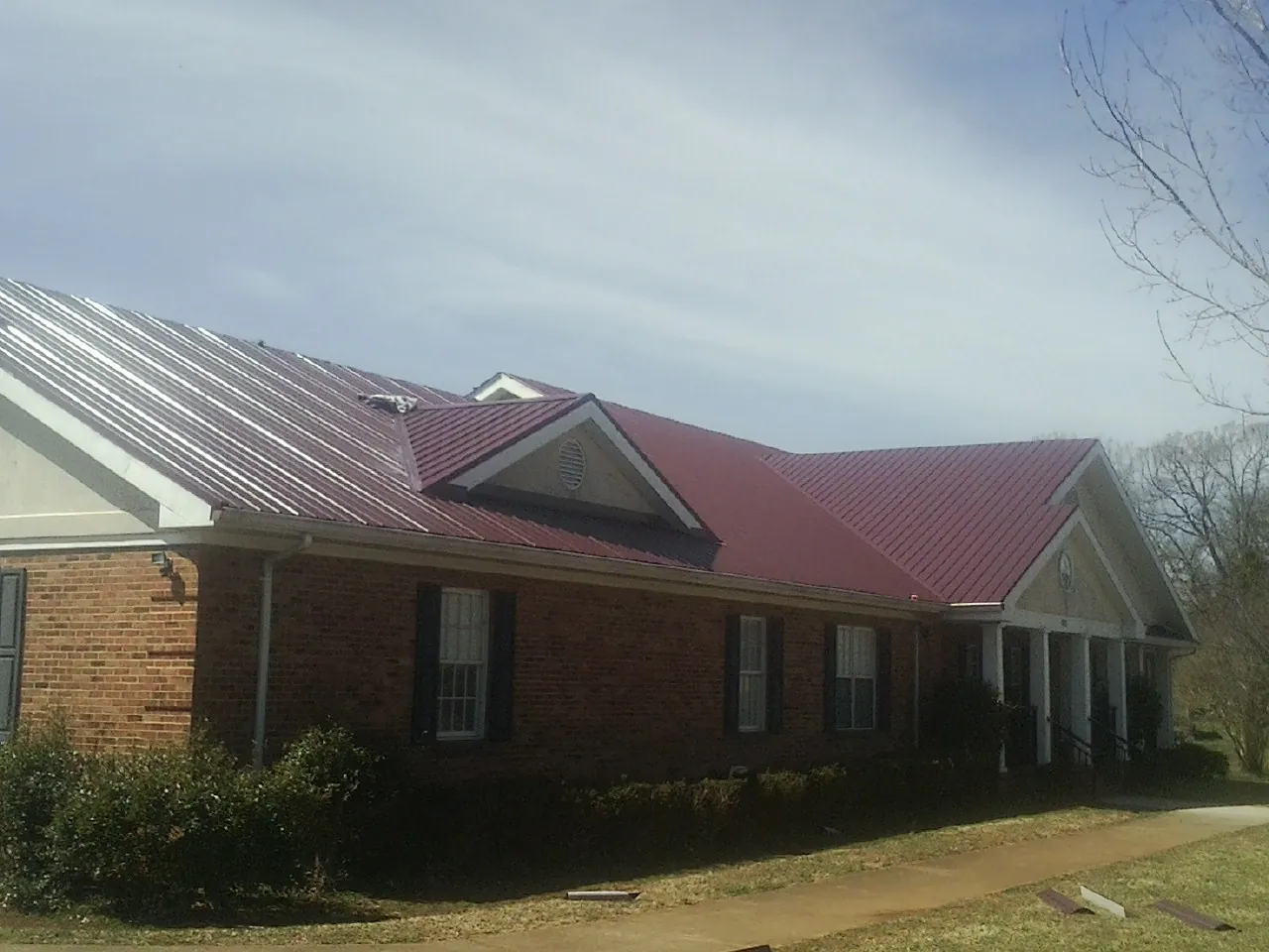 Red metal roof with gabled entries on a long brick building, from a Hail Damage Roof Repair job in Stafford